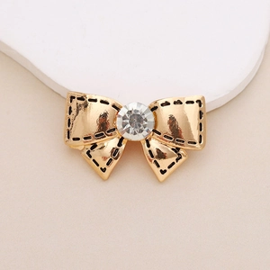 Detail of a golden bow charm with a crystal center and black dotted edges for DIY crafts