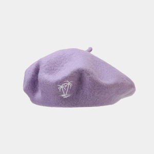 Close-up of a purple wool beret featuring detailed white palm tree embroidery texture