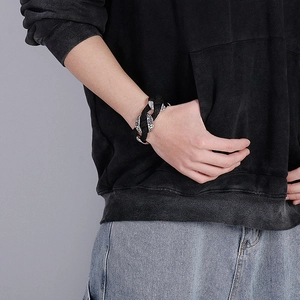 Detail of woven black leather bracelet with engraved silver metal charms on male wrist