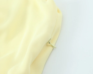 Close-up of invisible zipper closure on light yellow pleated woven midi dress fabric