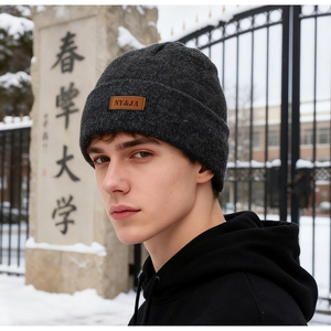 Outdoor close-up of dark grey knitted beanie with brown leather logo patch on winter background