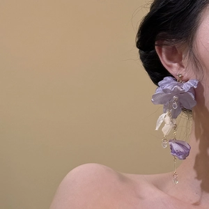 Eleganti orecchini a nappa con fiori in tessuto viola e cristalli su modella di profilo