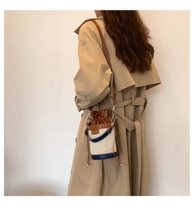 Detail of canvas bucket bag with leather trim worn by model in a trench coat