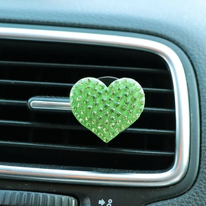 Macro shot of green rhinestone heart car air vent clip installed on interior dashboard