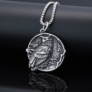 Detail of vintage silver owl relief pendant with stainless steel bead chain on dark surface