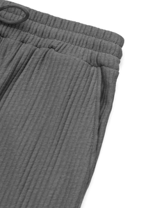 Detail of grey ribbed trousers showing elastic waistband, drawstring and pocket texture