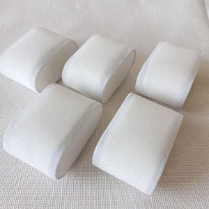 Five white velvet jewelry pillows for watches and bracelets on beige linen background