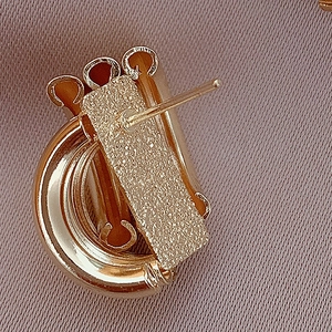 Detailed close-up of golden geometric earrings with brushed metal finish on pink fabric