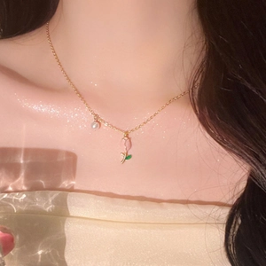 Detail of tulip pendant with pearls on a gold chain worn by a model in soft lighting