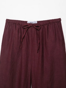 Detail of burgundy linen trousers featuring adjustable drawstring waist and natural texture