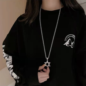 Close-up of a silver hexagram pendant on a long chain held against a black hoodie