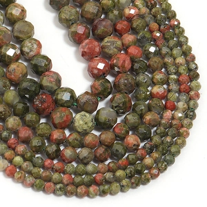 Macro shot of faceted green and red natural stone beads arranged in a U-shape on white