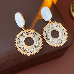 Detailed close-up of gold and white mesh circle drop earrings on a dark textured surface