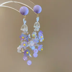 Detail of purple floral tassel earrings with beaded accents hanging on a clear display