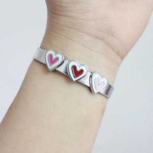 Silver metal bracelet with pink and red enamel heart charms on a wrist for daily accessory