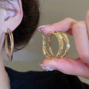 Detail shot of multi-layered golden crossover hoop earrings worn on a female model