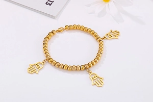 Detailed shot of golden bead bracelet with hollow Hamsa Hand charms on white background