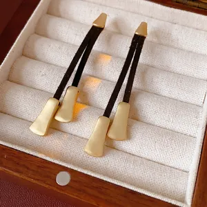 Elegant gold metal earrings with brown leather tassels in a wooden jewelry gift box