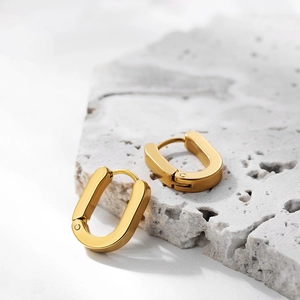 Detail of chunky 18K gold plated oval hoop earrings on natural white stone surface