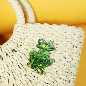 Acrylic green frog brooch with gold outlines and rhinestones on a beige straw bag