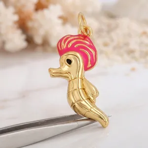 Détail d'un pendentif hippocampe doré avec des accents en émail rose sur un fond blanc pur