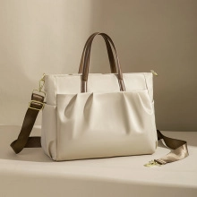 Detail view of a beige Boston bag with brown handles and a pleated front design
