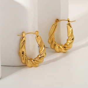 Artistic close-up of gold-plated twisted hoop earrings on white geometric block