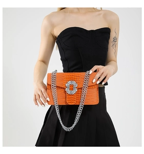 Detail of orange croc-effect handbag with sparkling rhinestone buckle and silver chain strap