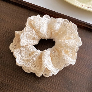 Détail d'un chouchou en dentelle brodée florale crème avec une texture douce à volants