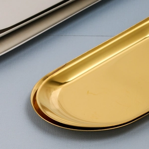 Polished golden oval stainless steel jewelry tray on a light blue textured surface