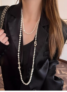 Detailed view of layered pearl necklace with zircon number five pendant on black suit