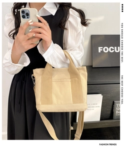 Detail of beige canvas tote bag showing front pocket and adjustable shoulder strap