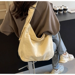 Cream canvas tote bag with wide strap shown on a model in a cozy cafe setting