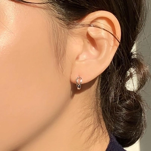 Macro shot of minimalist silver twisted hoop earring worn on an ear showing fine details