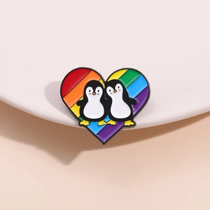 Close-up of a heart-shaped rainbow enamel pin with two cute cartoon penguins on a dish