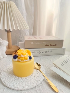 Artistic mango cake scented candle with realistic fruit toppings on a lace coaster