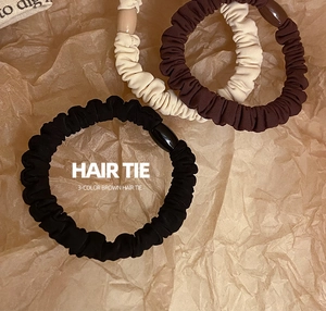 Close-up of three neutral fabric scrunchies in black, coffee, and beige on textured paper