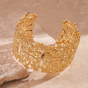 Détail du bracelet manchette doré large avec motifs floraux ajourés en dentelle fine