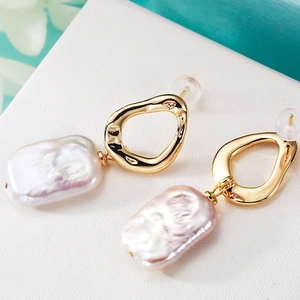 Baroque irregular freshwater pearl earrings with golden hoops on a clean white texture