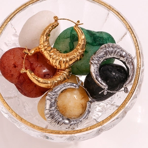 Macro shot of gold and silver hollow hoop earrings in a crystal bowl with colorful stones