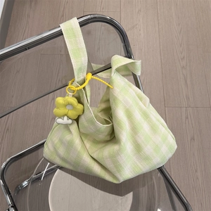 Detail of green and white checkered canvas tote bag with a yellow flower charm on a chair
