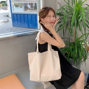 Minimalist cream canvas tote bag with large capacity, shown by a model near a window
