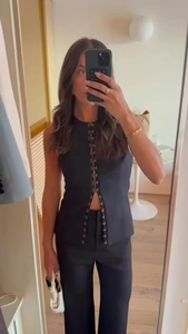 Detail of black sleeveless top with metal hook-and-eye closures and slim fit trousers