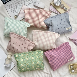 Variety of plaid and floral cotton makeup bags scattered on a cozy bed with accessories