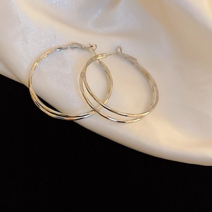 Macro detail of silver geometric hoop earrings with faceted texture on white silk fabric