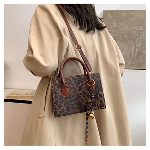 Chic leopard print tote bag featuring brown leather handles and gold bell charm detail