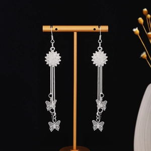 Detail of silver bohemian tassel earrings with flower and butterfly charms on a stand