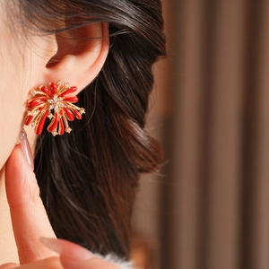 Vue rapprochée des boucles d'oreilles fleur dorées avec émail rouge et cristaux de zircone
