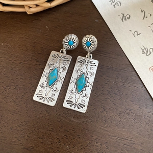 Macro detail of bohemian silver earrings with turquoise stones on vintage wood background