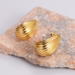 Macro detail of gold-plated teardrop earrings with linear texture on a stone base